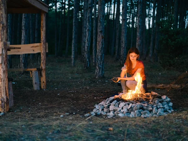 Žena poblíž táboráku venku ve večerních hodinách v borovém lese — Stock fotografie