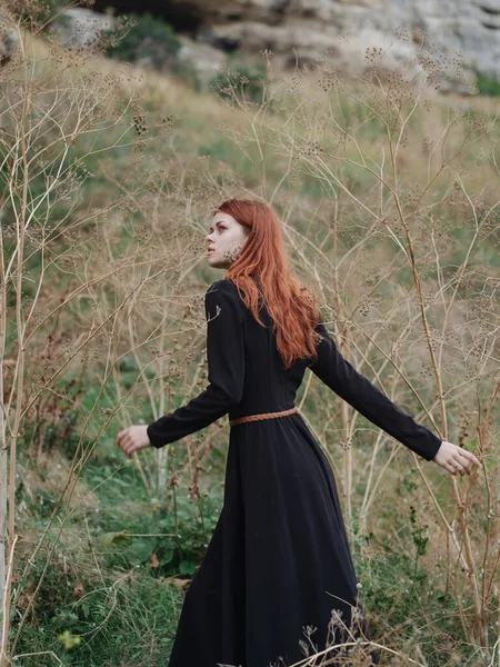 Mulher na floresta em um vestido preto cabelo vermelho natureza ar fresco — Fotografia de Stock