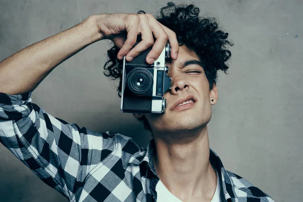 Chico guapo con una cámara cerca de su cara y pelo rizado camisa a cuadros fotógrafo hobby — Foto de Stock