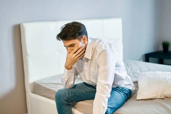 Overstuur man binnen op het bed raken van zijn gezicht met zijn hand eenzaamheid verdriet — Stockfoto