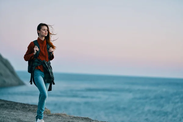 Mujer en jeans con una mochila en su espalda mar en el fondo y altas montañas —  Fotos de Stock