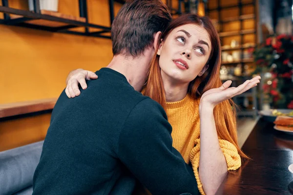 Mujer romántica abraza a un hombre joven en un suéter en una mesa en el interior de un café una pareja enamorada — Foto de Stock