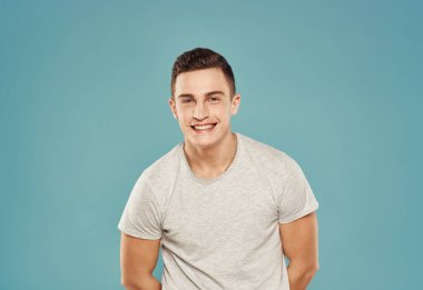 Tişört giymiş neşeli bir adam elleri mavi arka planda hareketler yapar.