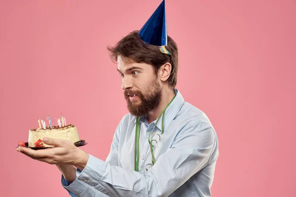 Un hombre con una camisa con un pastel en las manos y una gorra festiva en la cabeza — Foto de Stock