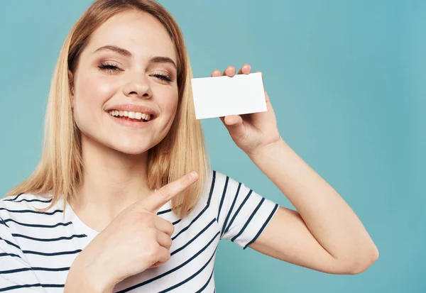 Una donna su uno sfondo blu in una maglietta a righe con un biglietto da visita in mano — Foto Stock