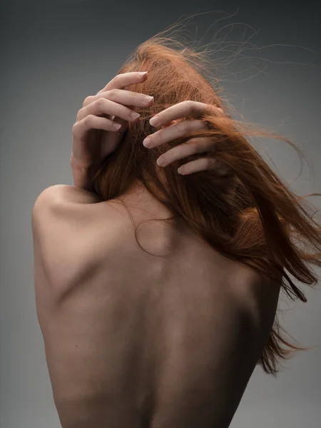 Back view of sexy red-haired woman naked back touching with hands