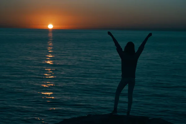 Femme dans les montagnes au coucher du soleil près de la mer leva les mains vers le haut — Photo