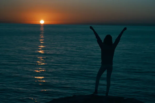 Woman in the mountains at sunset near the sea raised her hands up — Stock Photo, Image