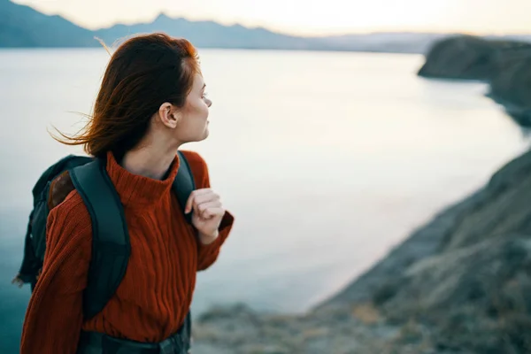Donna in un maglione vicino al mare in montagna guarda di lato e uno zaino sulla schiena — Foto Stock