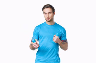 Hafif arka planda dambıllar ve mavi tişört dövmeli bir sporcu.