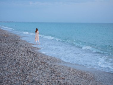 Okyanus kıyısında süveterli bir kadın ve berrak suyla mavi gökyüzü.
