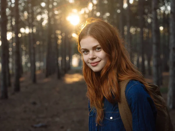 Šťastná žena v modré košili cestuje v borovém lese a západ slunce v dálce — Stock fotografie