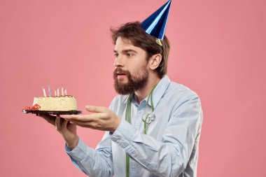 Ellerinde pasta ve kafasında şenlik şapkası olan tişörtlü bir adam.