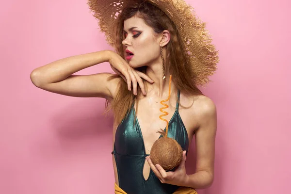 Kvinna med kokos cocktail i händerna baddräkt strand hatt kosmetika lyx livsstil rosa bakgrund — Stockfoto