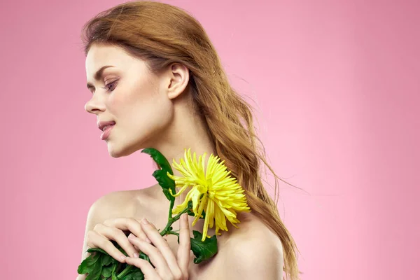 Piękna dziewczyna z żółtym kwiatem na różowym tle nagie ramiona makijaż — Zdjęcie stockowe