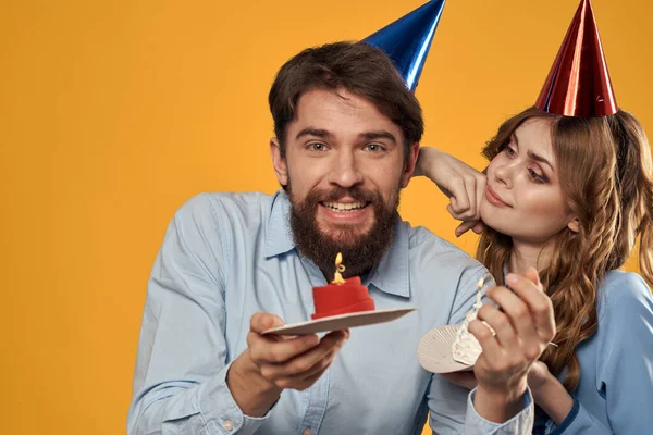 Birthday party man and woman in a cap with a cake on a yellow background cropped view — Stock Photo, Image