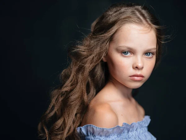 Retrato de una hermosa chica con el pelo rizado sobre un fondo oscuro, hombros desnudos y un vestido azul — Foto de Stock