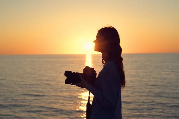日落时分在海边带着相机的女人的轮廓 — 图库照片