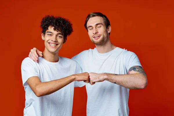 Twee vrienden in witte t-shirts knuffels communicatie rode achtergrond — Stockfoto