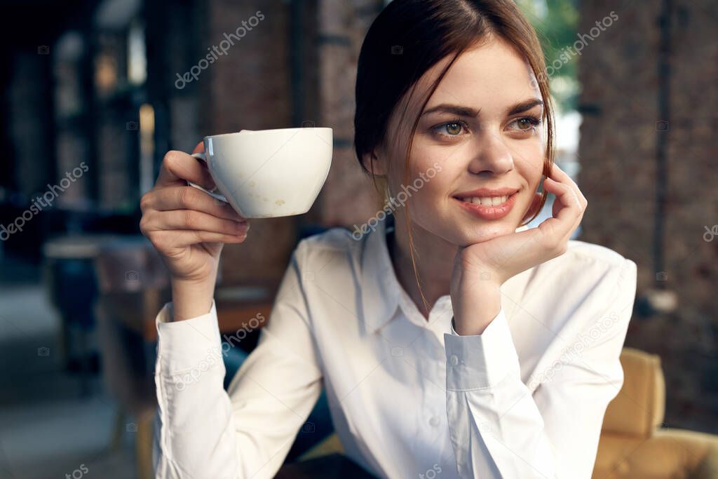 pretty business woman in white shirt sits in a cafe with a cup of coffee. High quality photo