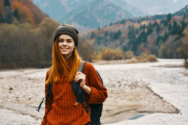 woman in a sweater and  hat with a backpack resting near the river in the mountains