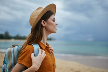 Sırtında sırt çantasıyla bereli bir kadın deniz kenarındaki kumsalda doğaya bakıyor.