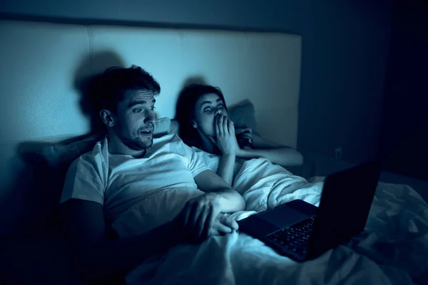 Mladý pár ležící na posteli v noci před notebookem — Stock fotografie