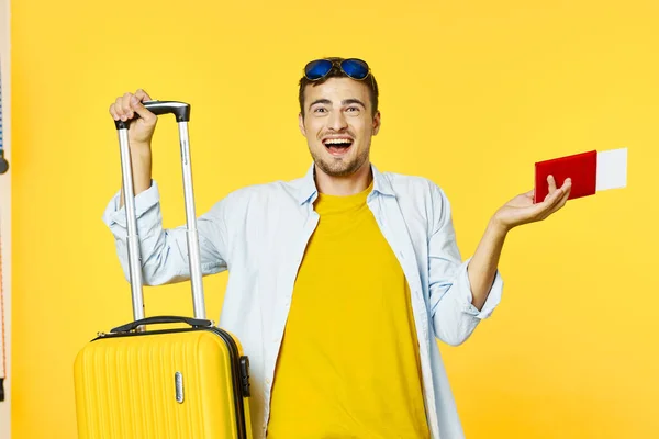 man with suitcase on yellow background and passport plane tickets travel tourism