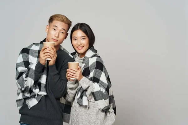 Un homme et une femme avec une couverture chaude sur leurs épaules tenant du café chaud dans leurs mains sur un fond gris — Photo
