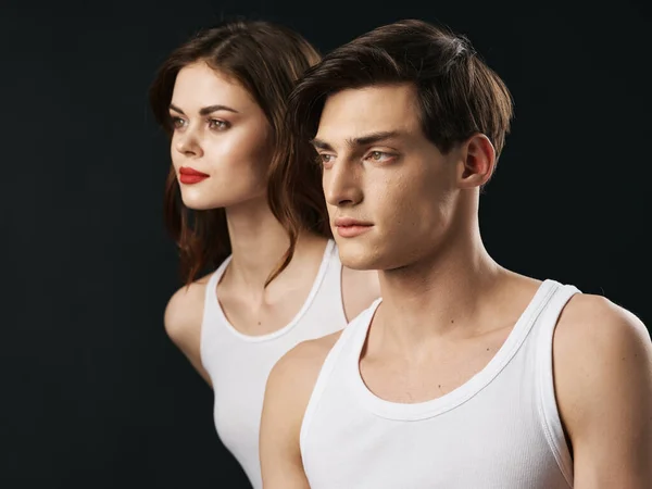 Uomo e donna in t-shirt bianche su sfondo scuro guardando lateralmente vista ritagliata — Foto Stock