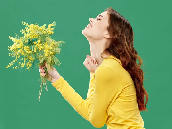 Woman with a branch of yellow pussy willow on a green background smile side view — Stock Fotó