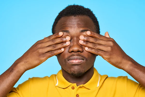 Homem africano em camiseta amarela com olhos fechados em fundo azul — Fotografia de Stock