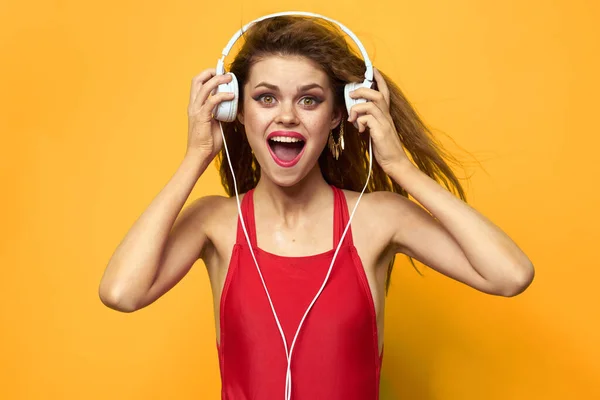 Веселая женщина в наушниках слушает музыку в красной футболке на жёлтом фоне — стоковое фото