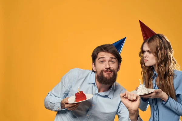Aniversário festa homem e mulher em um boné com um bolo em um fundo amarelo vista cortada — Fotografia de Stock