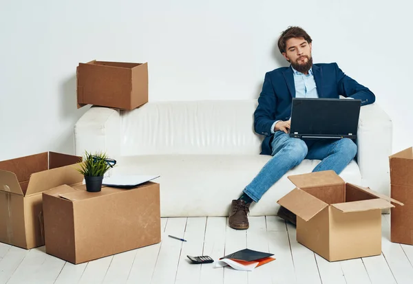 Man sitting on sofa with laptop office boxes with things work