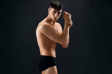 Kabarık kaslı vücudu olan, koyu tenli arka planda poz veren bir adam.