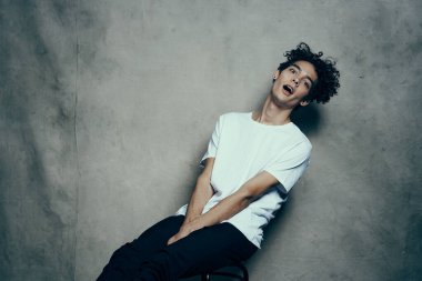 Kıvırcık saçlı genç kapalı bir sandalyede oturuyor.