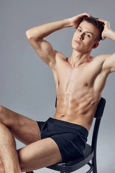 Handsome athletic man with pumped up abs sits on a chair and behind his head — Stock Photo, Image