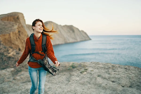 Жінка в червоному светрі з рюкзаком на спині на відкритому повітрі біля моря в горах Копіювати Простір — стокове фото