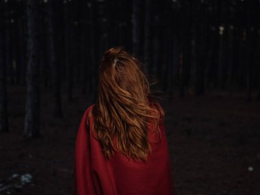 Omuzlarında kırmızı bir ekoseyle geceleri ormanda dolaşan bir kadın.