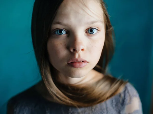 Porträtt av en vacker liten flicka i en grå klänning på en blå bakgrund närbild beskärd bild av modellen — Stockfoto