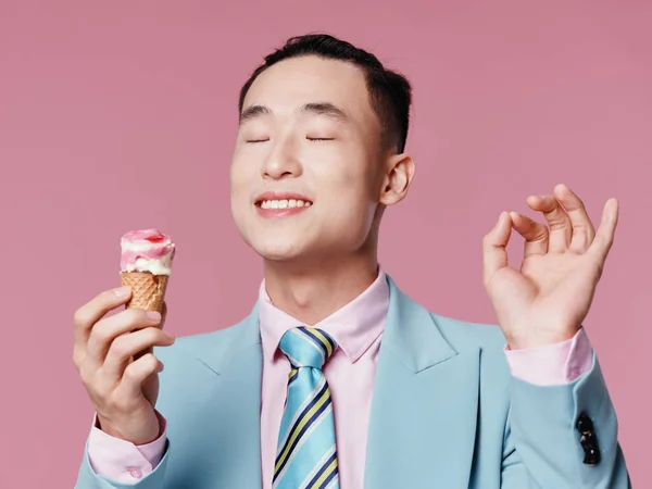 Ázsiai férfi csukott szemmel egy rózsaszín háttér fagylalt a kezében kóstoló — Stock Fotó