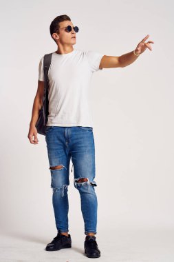 Sırt çantalı, kot pantolonlu, uzun spor ayakkabılı ve gözlüklü bir adam.
