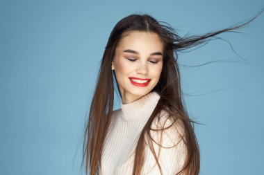 Beyaz kazaklı esmer, kırmızı dudaklı, uzun saçlı, mavi arkaplan.