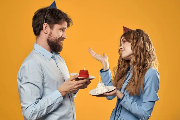 Födelsedag fest man och kvinna i en mössa med en kaka på en gul bakgrund beskärd vy — Stockfoto