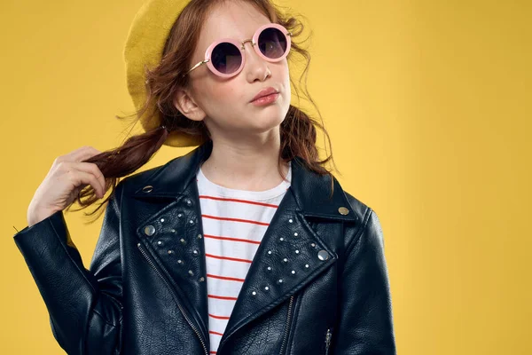 Güneş gözlüklü ve şapka takan neşeli küçük kız stüdyo sarı arka plan modası — Stok fotoğraf