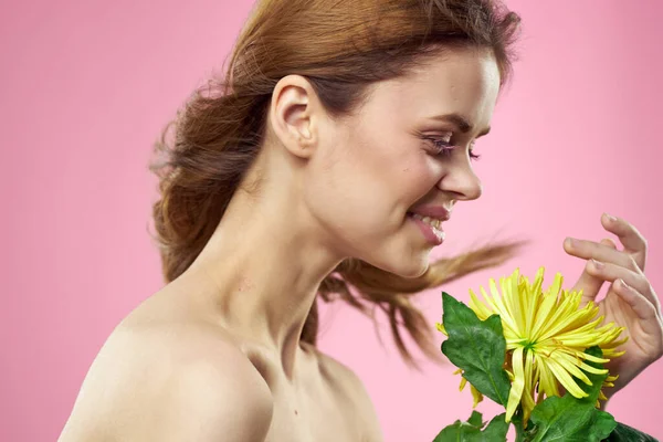 Hermosa mujer con hombros desnudos y una flor amarilla en sus manos sobre un fondo rosa — Foto de Stock
