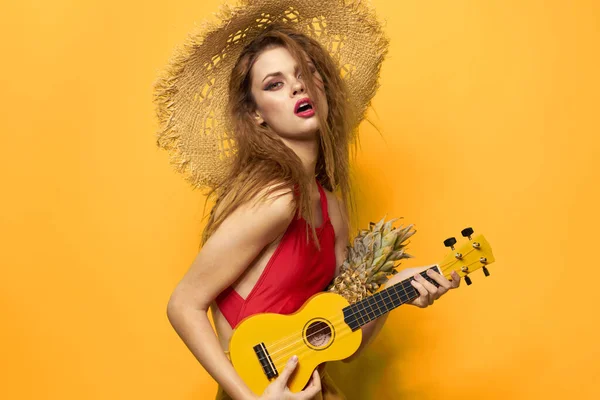Kobieta w czerwonym kapeluszu ukulele w rękach styl życia lato czerwony t koszula żółty tło — Zdjęcie stockowe