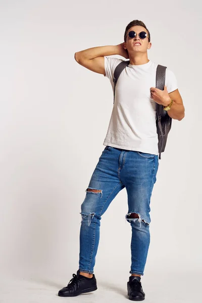 Een man met een rugzak op zijn rug in jeans t-shirt full length sneakers en bril op zijn gezicht — Stockfoto