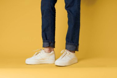 Kadınların bacakları kot pantolonlar beyaz spor ayakkabılar moda tarzı sarı arka plan